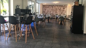 A modern dining area with black chairs and tables, a kitchen area with wine bottles, and a large mural on the wall. - Hôtel la clé (Saint-Andre-de-Sangonis)