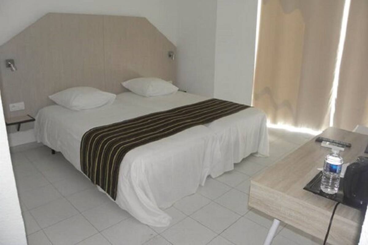 A hotel room with a bed, a nightstand, a wooden desk, and a curtain.