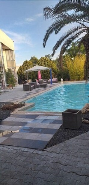 A swimming pool with a tiled deck, lounge chairs, and a covered seating area. - Hôtel la clé (Saint-Andre-de-Sangonis)