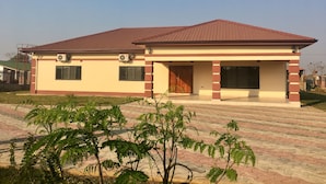A two-story building with a tiled roof, a covered porch, and a paved driveway. - Makeni Villa (Lusaka)
