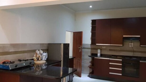 A modern kitchen with dark cabinetry, a central island, a built-in oven, and a microwave. - Makeni Villa (Lusaka)