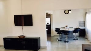 A modern kitchen with a dining area, a TV mounted on the wall, and a visible clock. - Makeni Villa (Lusaka)
