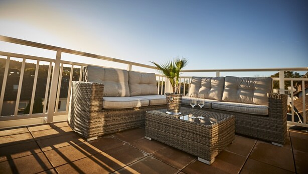 A balcony with wicker furniture, including a sofa and a coffee table, and a potted plant.
