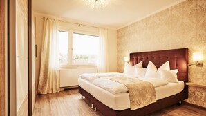 A hotel room with a large bed, a chandelier, and a window with curtains.