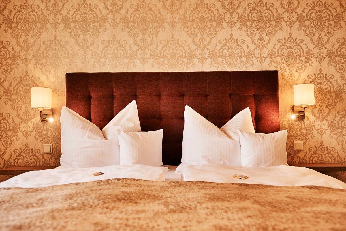 Una habitación de hotel con una cama grande, dos lámparas de noche y un papel tapiz estampado.