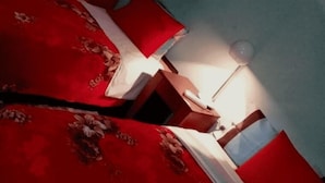 Una habitación con una colcha roja y una mesita de noche con una lámpara.