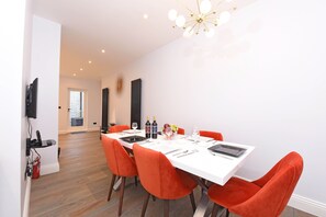 Uma área de refeições com uma mesa branca, cadeiras laranja e um candelabro.