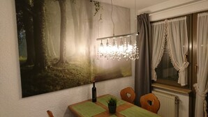 A dining area with a table, chairs, a chandelier, a large painting, and a window with curtains. - Residenz Schauinsland (Todtnau)