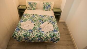 A neatly made bed with a tropical leaf pattern bedspread, two pillows, and two towels on the bed.