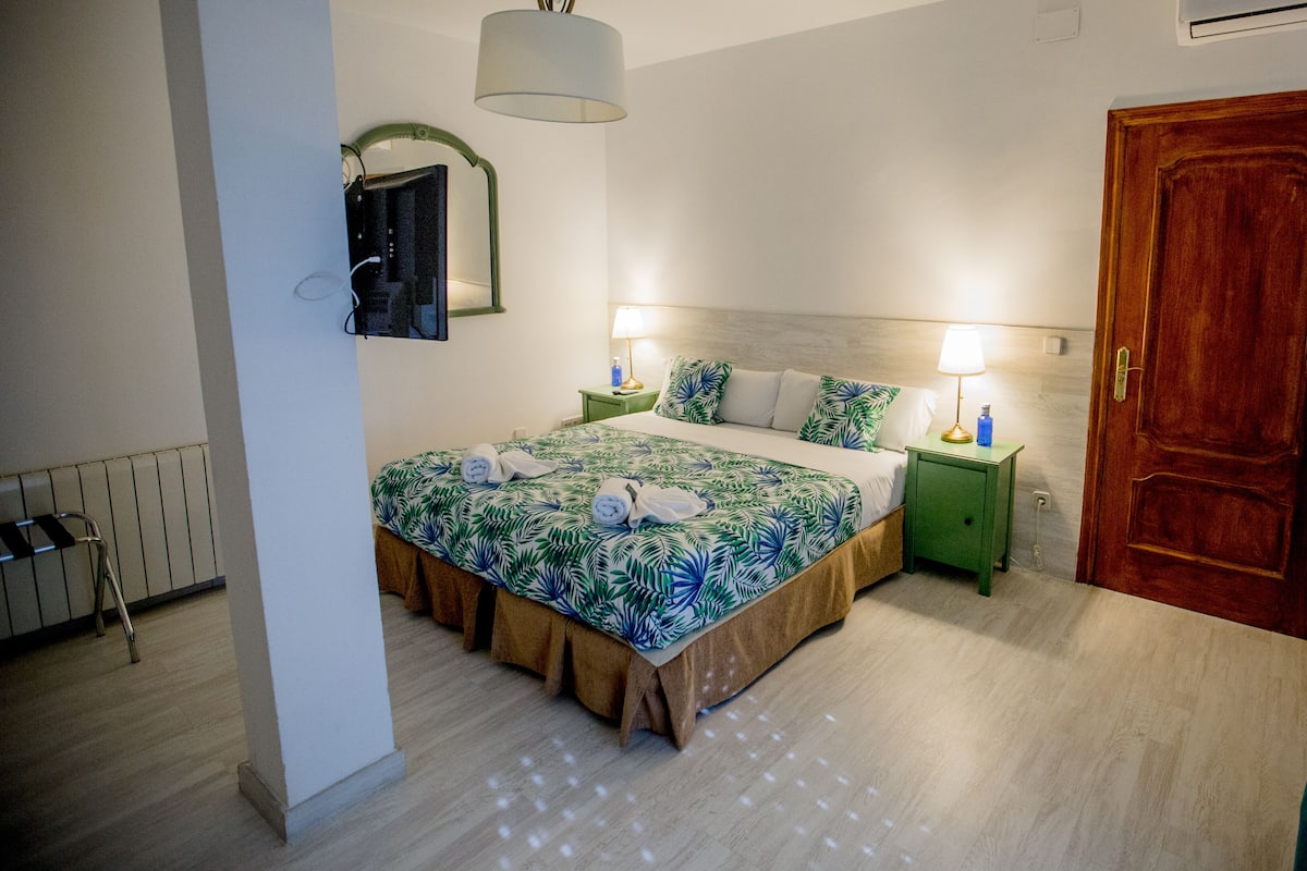 A hotel room with a bed, two bedside tables, a wooden door, and a radiator.