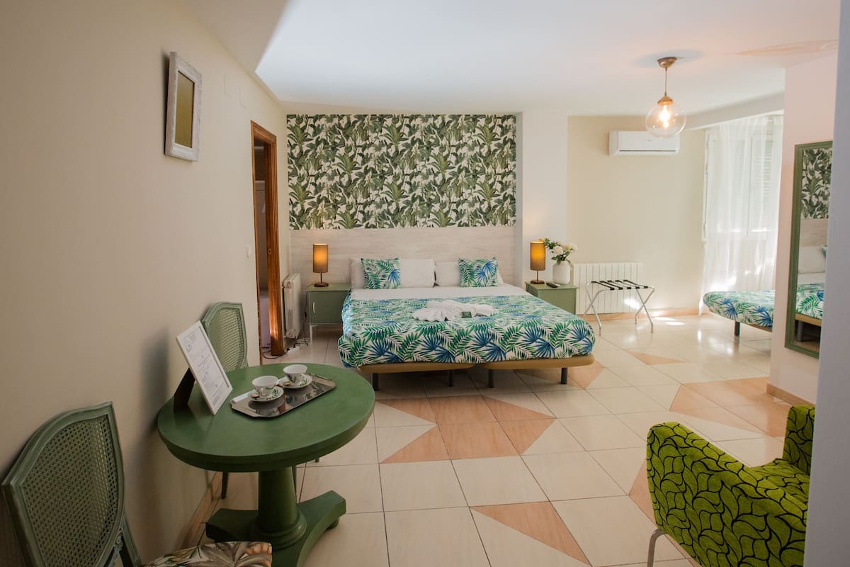 A hotel room with a bed, a dining table, a chair, a small table with a menu, and a mirror.