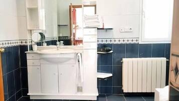 A bathroom with a white sink, mirror, and cabinets, a towel rack, and a radiator.