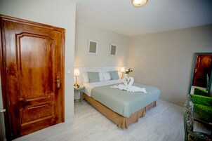 Egy hálószoba, fa ajtóval, zöld ágytakaróval borított ággyal, két éjjeliszemlivel, melyeken lámpák állnak, és egy tükör a falon.