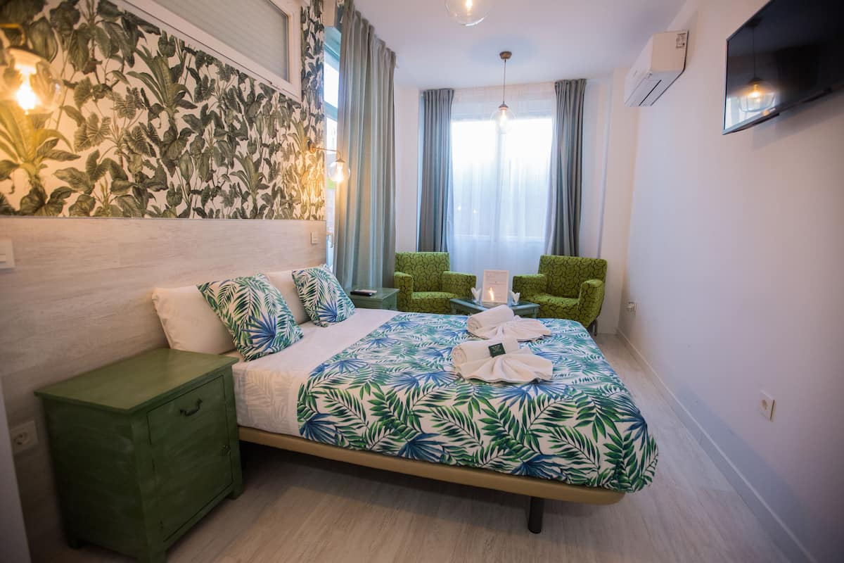 A hotel room with a bed, a green nightstand, a green chair, and a TV on the wall.