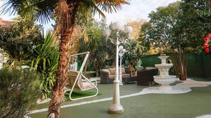 Un jardín con una mecedora, un farol blanco y una fuente.
