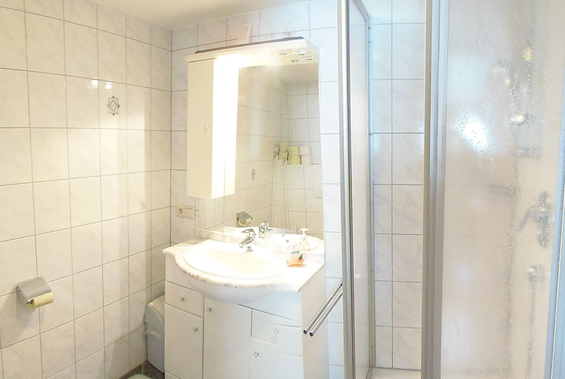 A bathroom with a white sink, mirror, and shower enclosure.