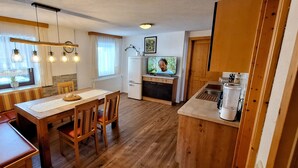 A cozy kitchen with wooden flooring, a dining table with chairs, a built-in oven, a refrigerator, and a television on the wall. - Schattaugut (Eben im Pongau)