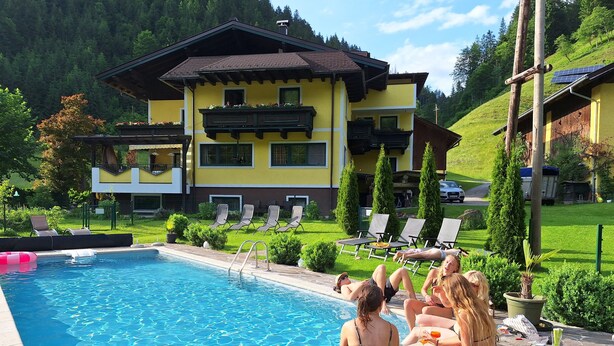 A swimming pool with lounge chairs, a building with balconies, and a mountainous backdrop. - Schattaugut (Eben im Pongau)