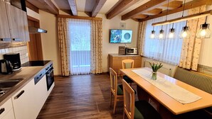 A kitchen with wooden cabinets, a microwave, and a dining area with a table and chairs. - Schattaugut (Eben im Pongau)