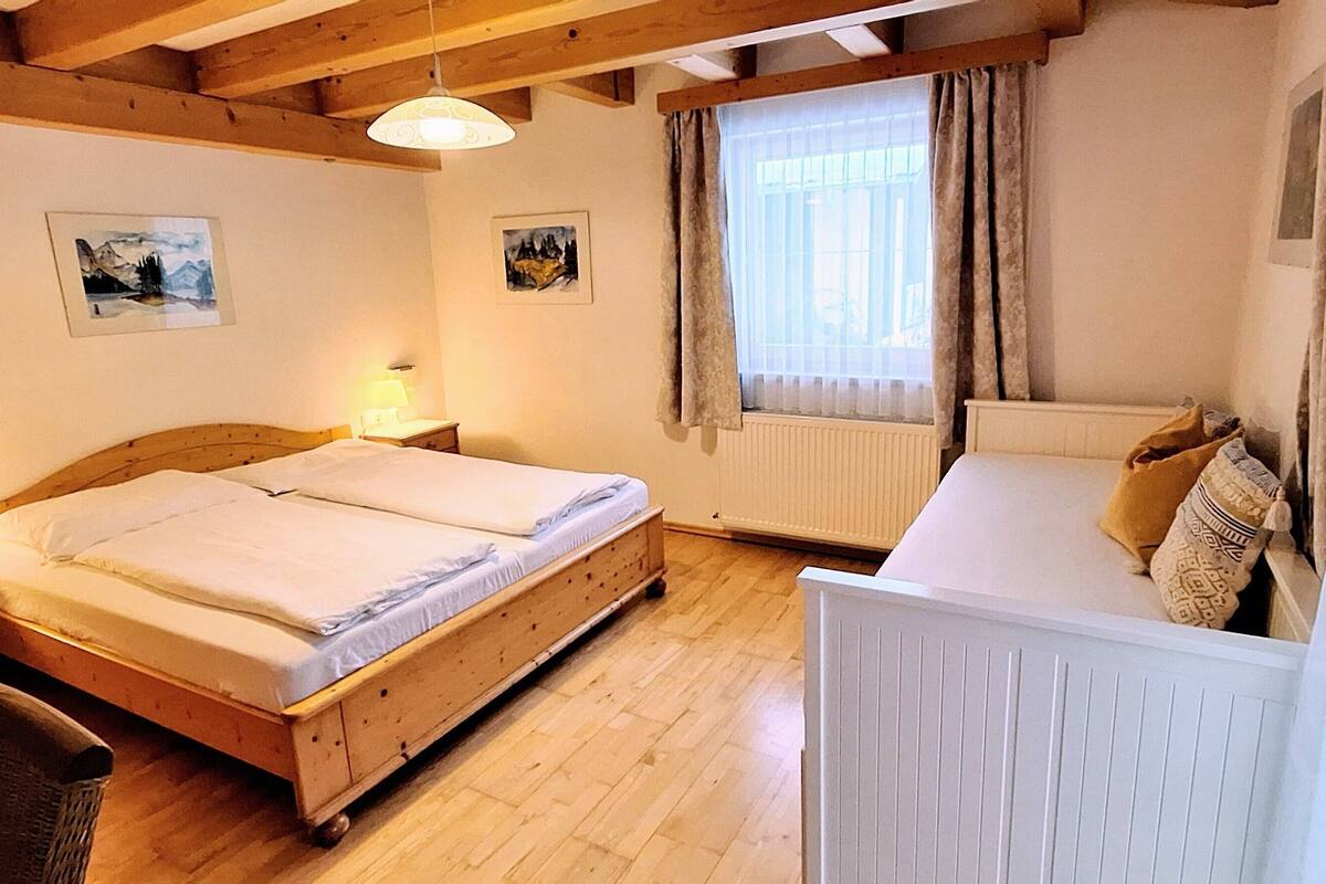 A room with a wooden bed, a chair, a radiator, and two paintings on the wall.