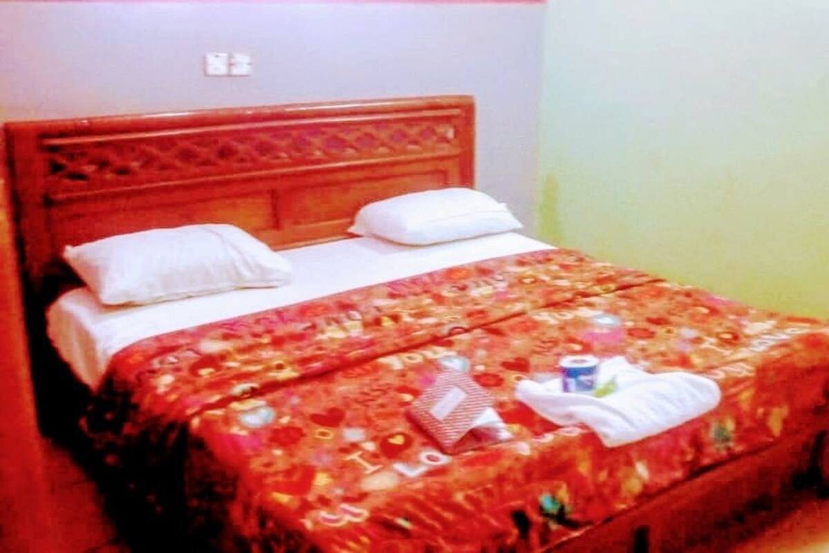 A bed with a floral bedspread, two pillows, and a small bedside table with a bottle and a tissue box.