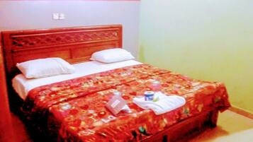 Una cama con cubrecama floral, dos almohadas y una mesita de noche con una botella y una caja de pañuelos.