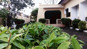 A building with a large entrance, surrounded by greenery and a fence. - Pride Garden Hotel (Calabar)