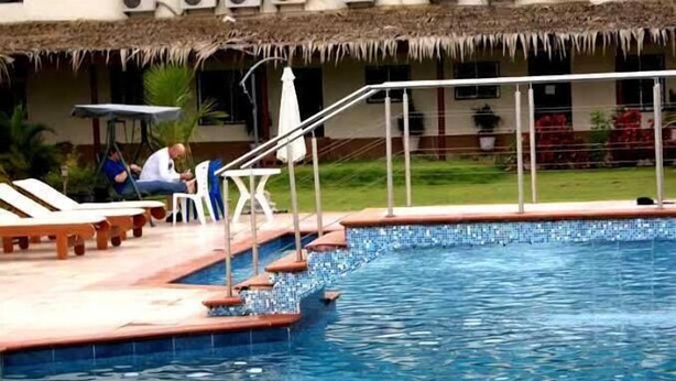 A swimming pool with a tiled edge, lounge chairs, and a thatched-roof building in the background. - Pride Garden Hotel (Calabar)