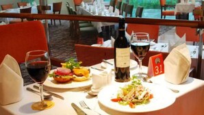 A dining table set with a burger, salad, wine glasses, and a bottle of wine. - Pride Garden Hotel (Calabar)