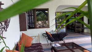 A room with a sofa, a small table, a patterned chair, and a window with a view of palm trees. - Pride Garden Hotel (Calabar)