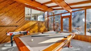 A pool table in a room with wooden walls and large windows.