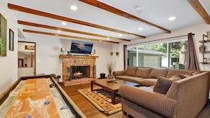 A cozy living room with a fireplace, a large sofa, a shuffleboard table, and a television.