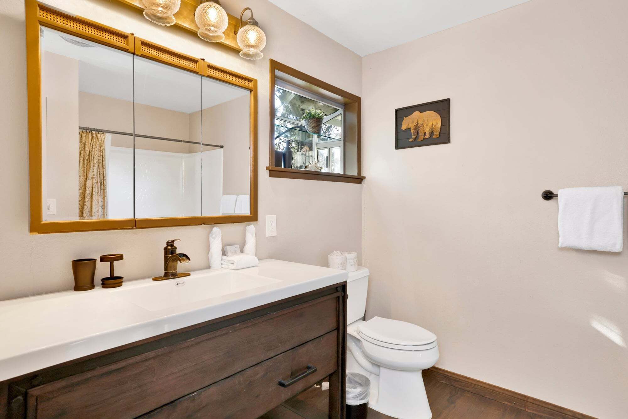 A bathroom with a large mirror, a white sink, a toilet, and a wall-mounted light fixture.