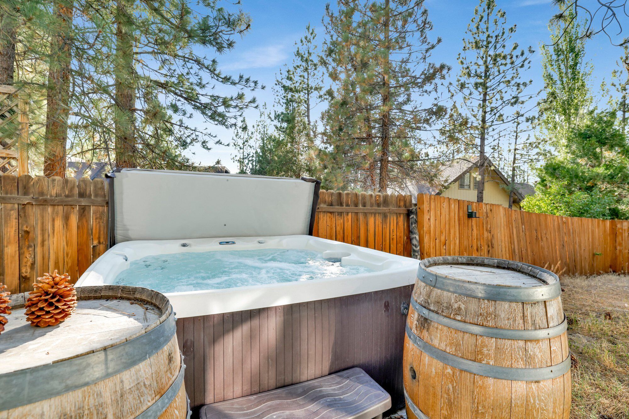 A hot tub with a wooden deck, two wooden barrels, and a wooden fence in a backyard.