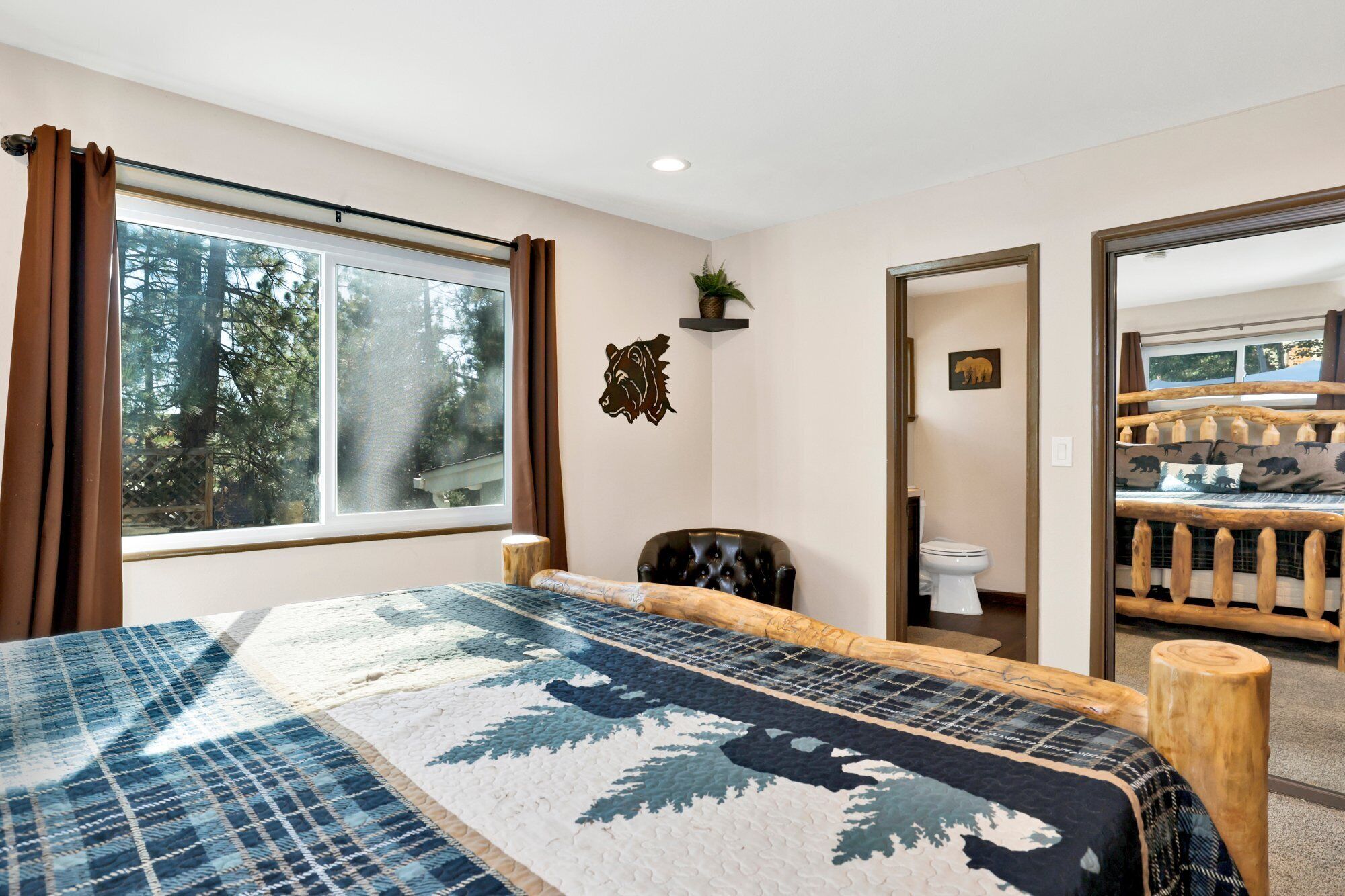 A bedroom with a large bed, a window with curtains, a bear-themed wall decoration, and a view of a wooden deck with a sofa.