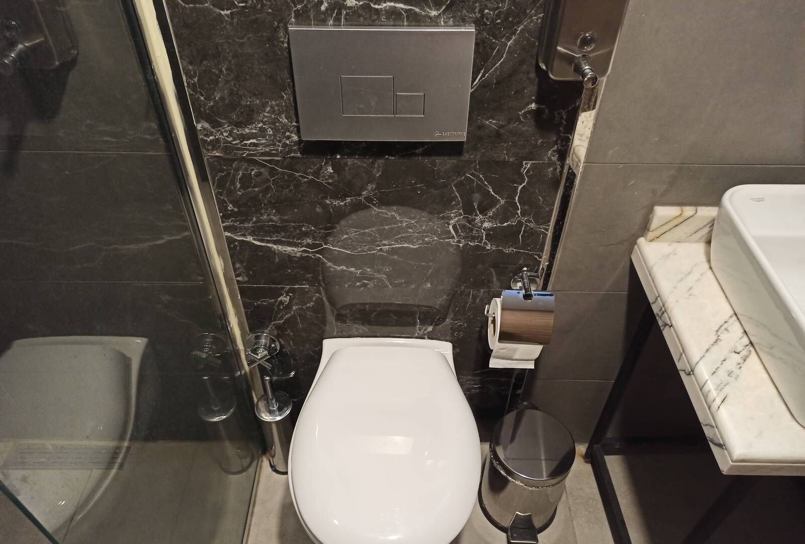 A bathroom with a toilet, a bidet, a glass shower enclosure, and a marble countertop.