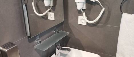 A modern bathroom with a white sink, a mirror, and two hair dryers mounted on the wall.