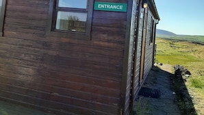 A wooden building with an 'ENTRANCE' sign, a window, and a view of a green landscape. - Guesthouse Hagi 1 (Husavik)