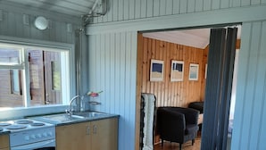 A compact kitchen with wooden cabinets, a stove, and a sink. There is a dining area with a table and chairs visible through an open door. - Guesthouse Hagi 1 (Husavik)