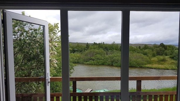 A view from a balcony with a wooden railing, overlooking a river and greenery. - Guesthouse Hagi 1 (Husavik)