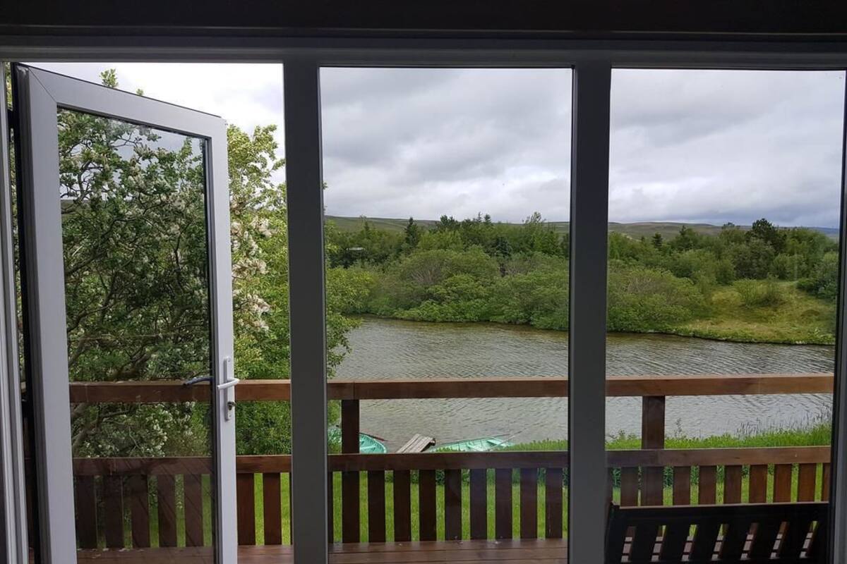 A view from a balcony with a wooden railing, overlooking a river and greenery.