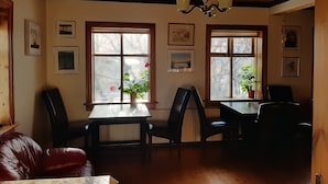 A dining area with wooden ceiling and walls, two windows with plants, and framed pictures on the walls. - Guesthouse Hagi 1 (Husavik)