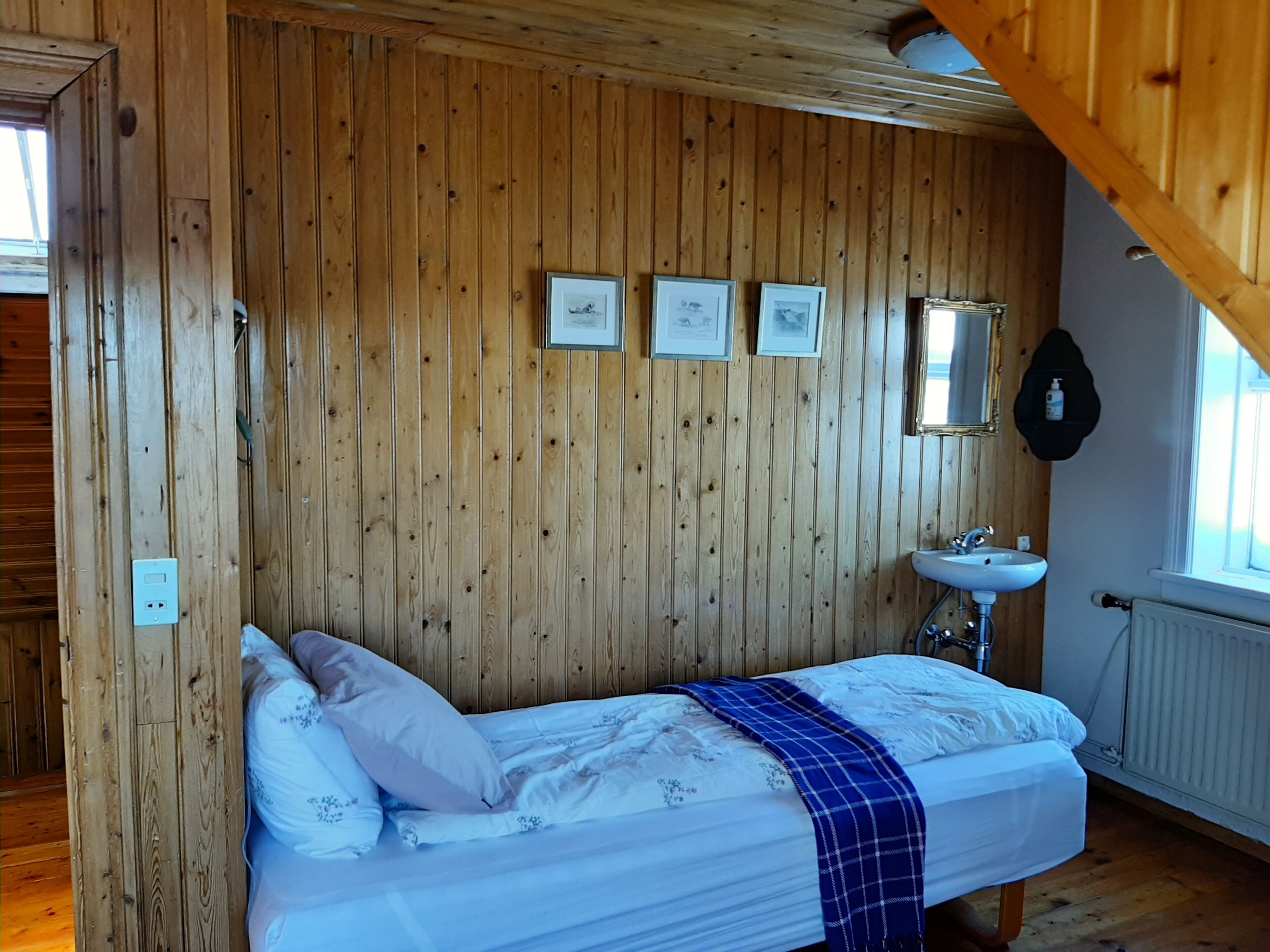 A wooden-paneled room with a bed, a wall-mounted mirror, and a small sink.