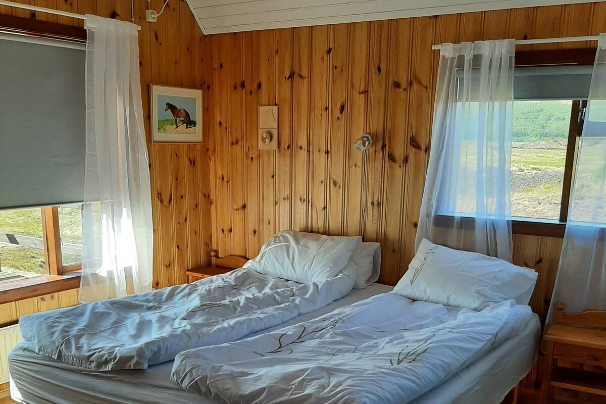 A wooden-paneled room with a bed, a small table, and a chair.