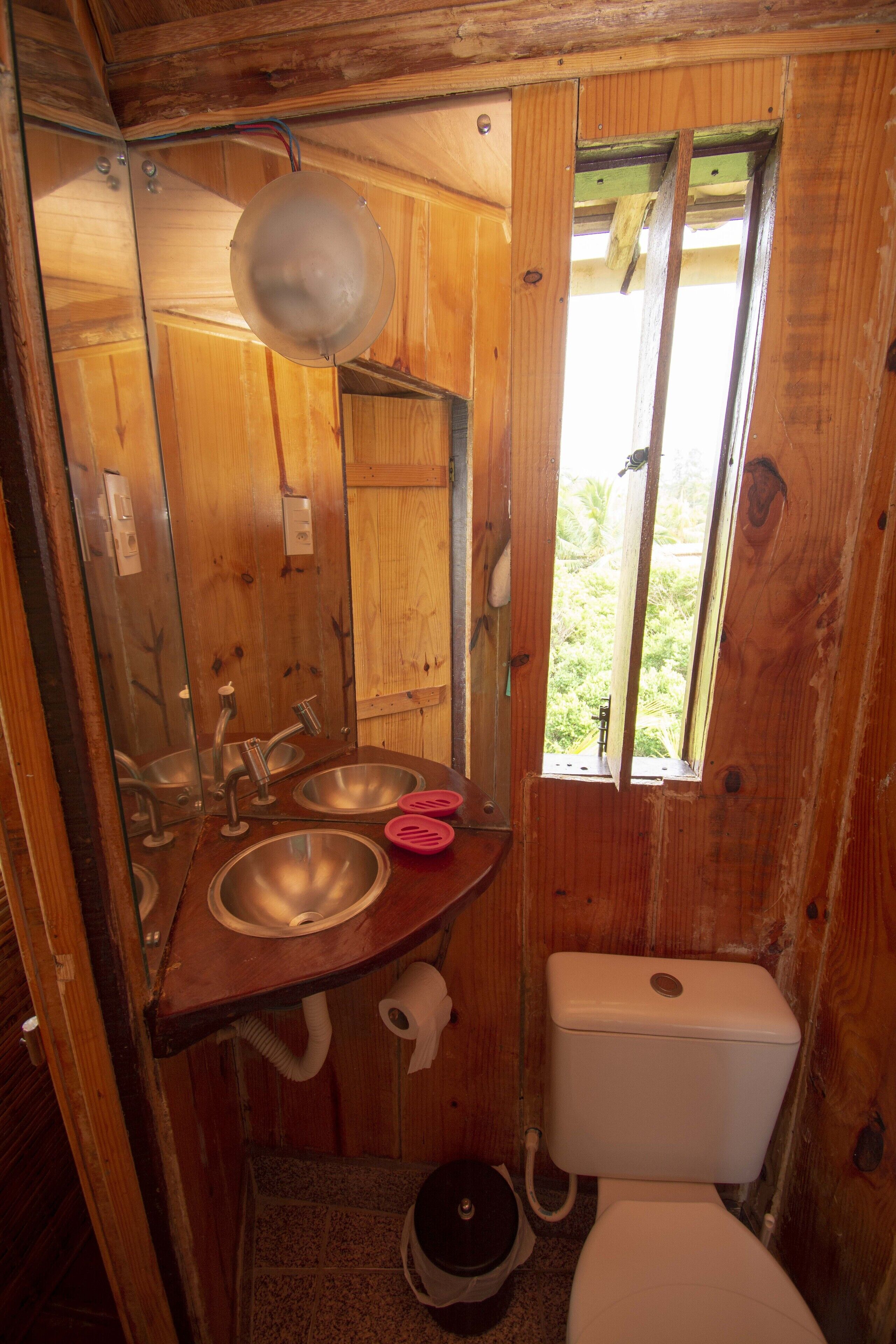 Une petite salle de bain en bois, équipée d’un lavabo, d’un miroir et de toilettes.