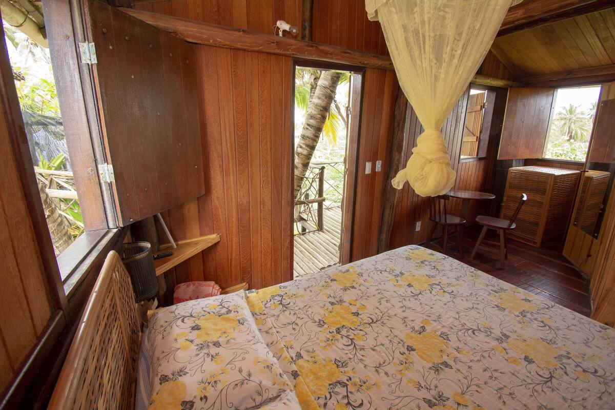 A wooden room with a bed, a small table, and a chair.