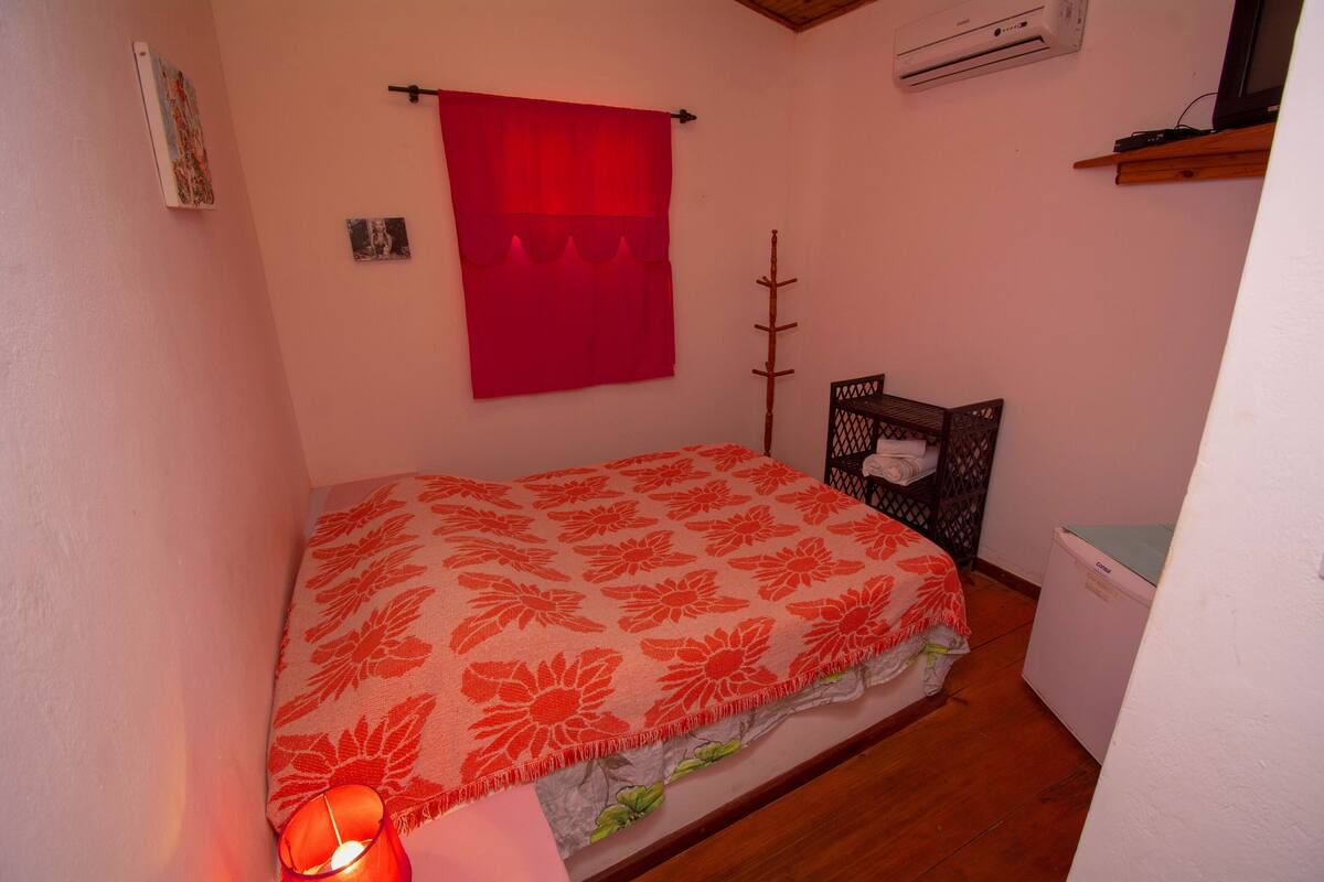 A small bedroom with a bed, a red curtain, a heater, and a small white appliance.