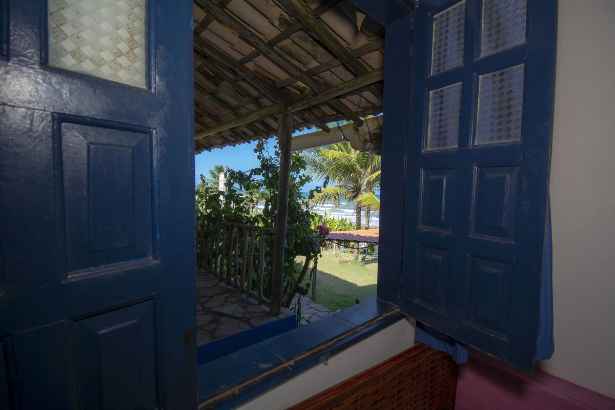 A view from a blue door into a covered outdoor area with a palm tree and a small garden.
