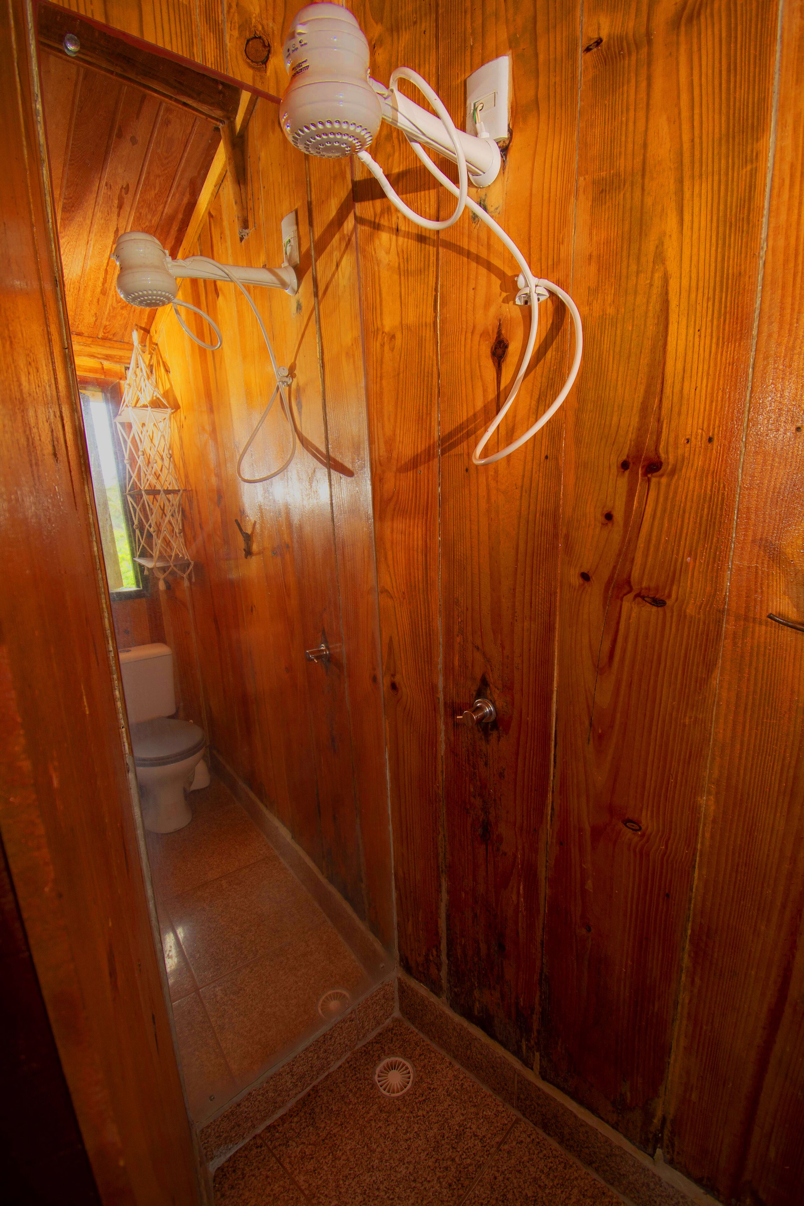Un baño de madera con ducha, inodoro y un secador de pelo fijado a la pared.