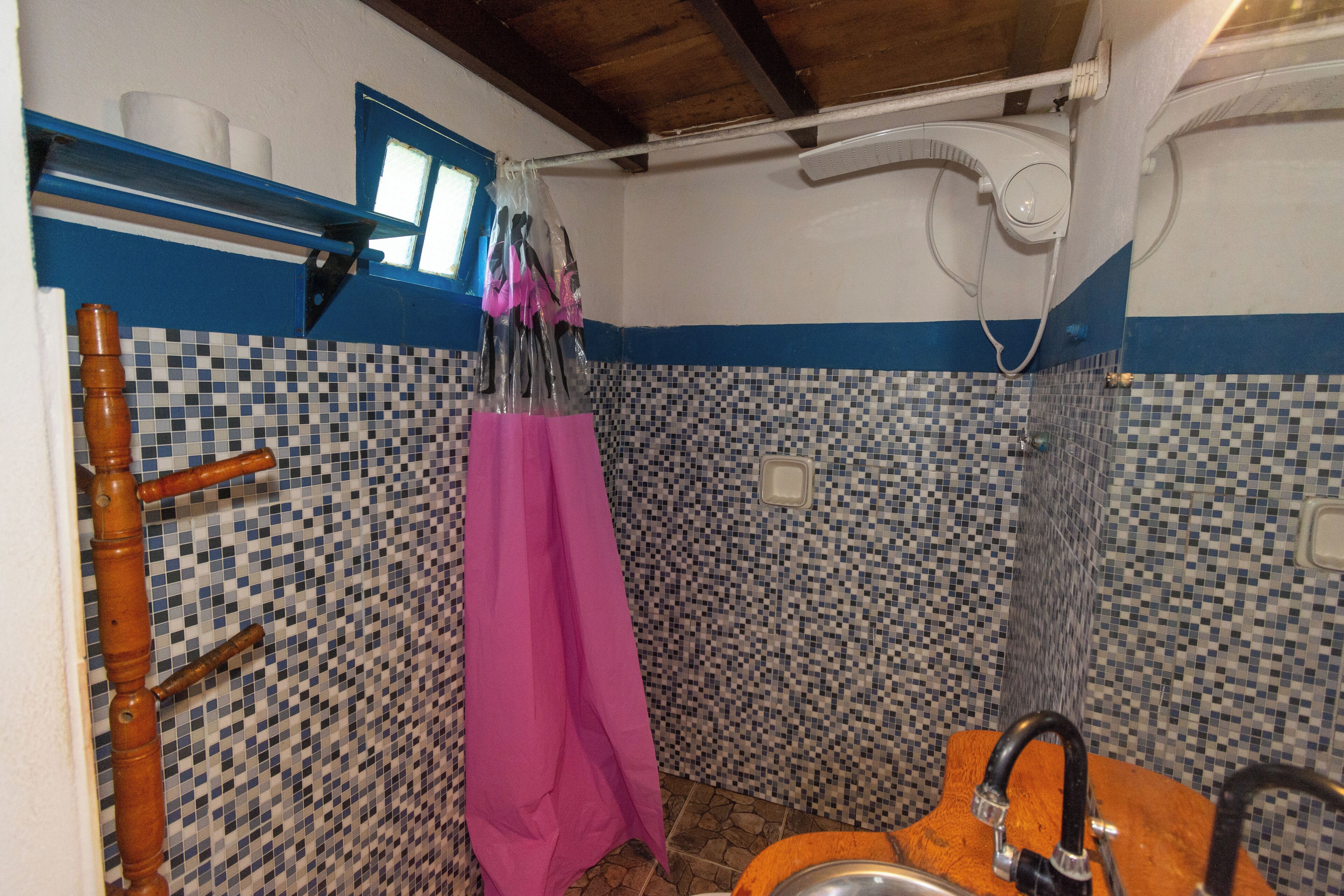 A bathroom with a tiled mosaic wall, a wooden towel rack, a pink towel, and a shower with a wooden seat.